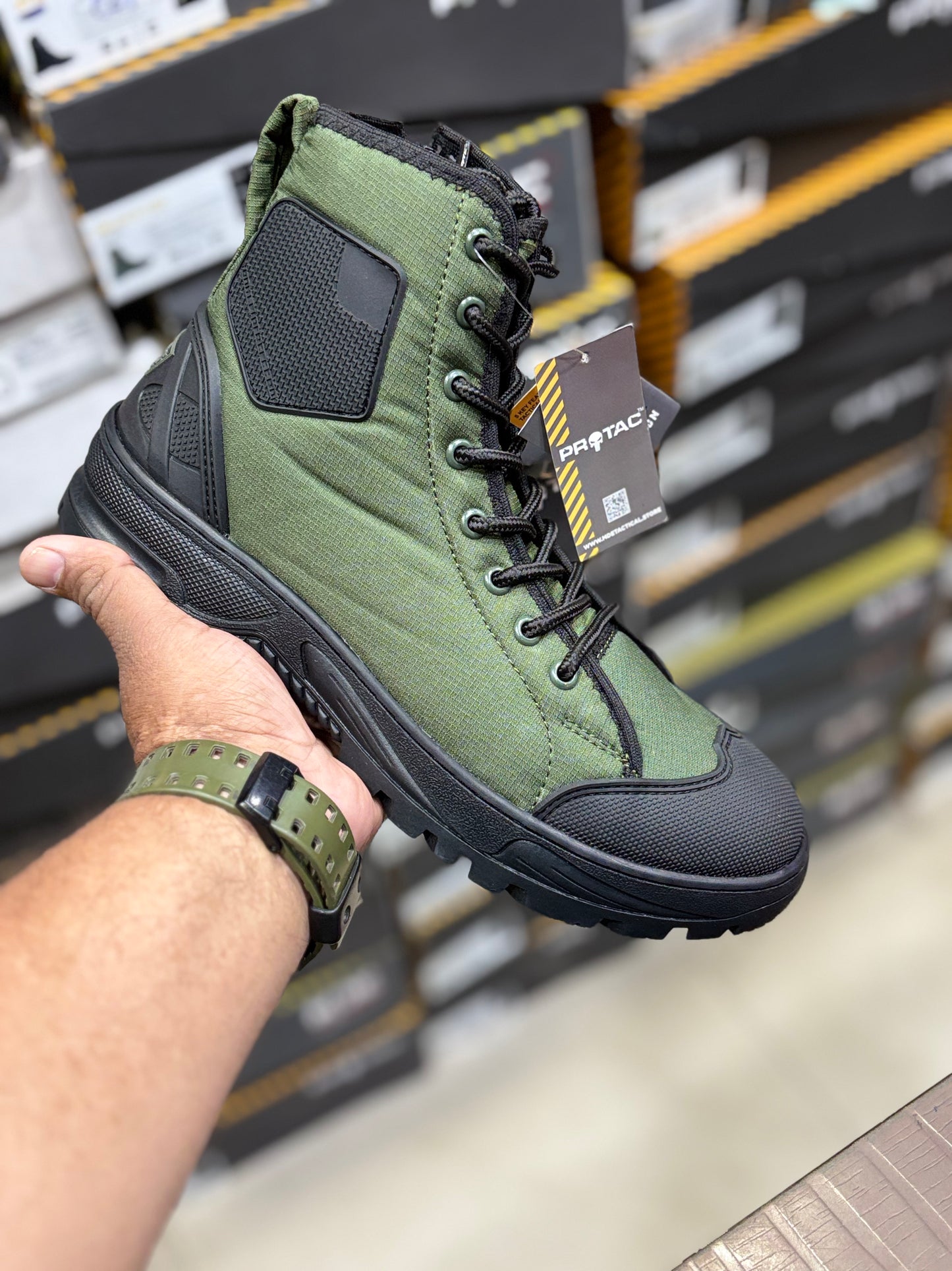Green and black hiking boot held by a person with a blurred store shelf in the background