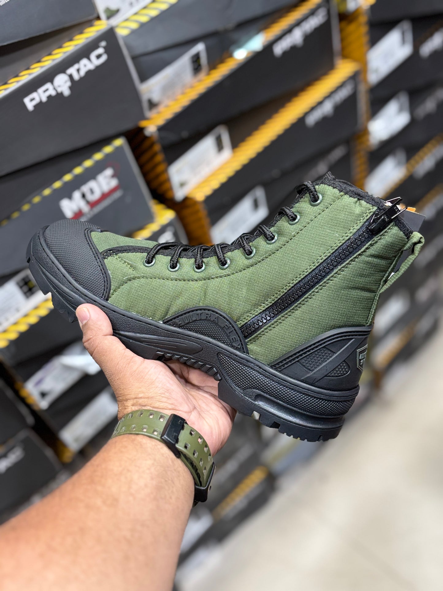 PROTAC RAPTOR Hunter 2.0 Green hiking boot with black sole held by a hand in front of shoe boxes